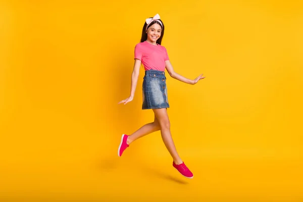 Zdjęcie uroczej uczennicy ubrany różowy t-shirt skoki wysokie spacery uśmiechnięty odizolowany żółty kolor tła — Zdjęcie stockowe