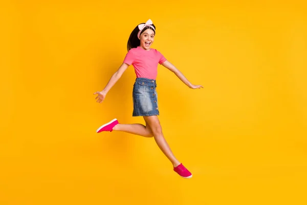Bild av imponerad glänsande skola flicka bära rosa t-shirt leende hoppa högt isolerad gul färg bakgrund — Stockfoto