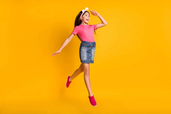 Foto van glanzend opgewonden schoolmeisje dragen roze t-shirt springen arm voorhoofd kijken ver weg lege ruimte geïsoleerde gele kleur achtergrond — Stockfoto