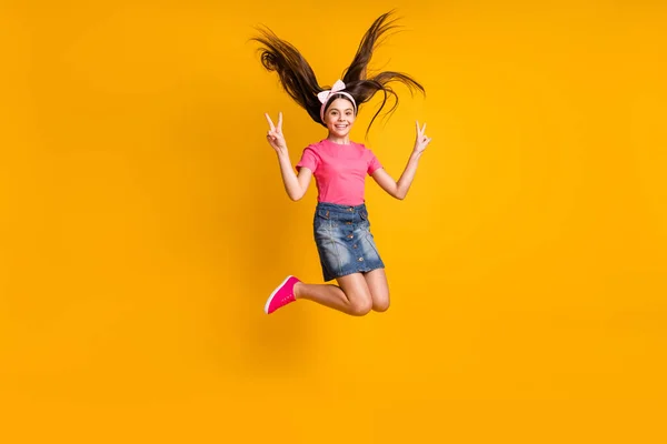 Photo of sweet charming schoolgirl dressed pink t-shirt jumping high showing two v-signs smiling isolated yellow color background — Stock Photo, Image