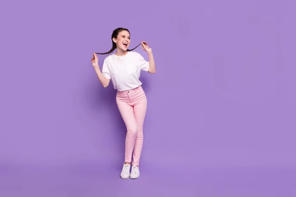 Foto de comprimento total de menina animada feliz sorriso positivo segurar tranças olhar espaço vazio isolado sobre fundo cor violeta — Fotografia de Stock