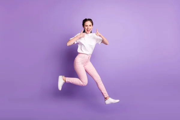 フルボディ写真の幸せなファンキー若いです女性ジャンプアップ笑顔作り親指アップ絶縁上の紫色の背景 — ストック写真