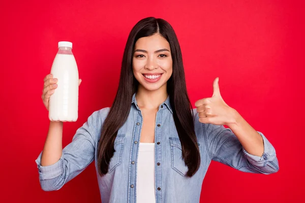Portrait of attractive cheerful girl holding fresh bio milk bottle showing thumbup ad isolated over bright red color background — Stock Photo, Image