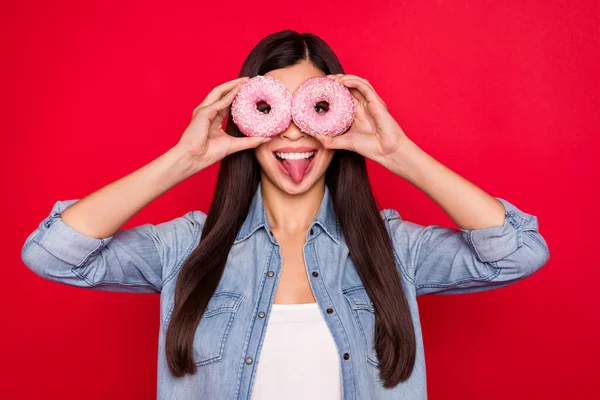 Portrait d'attrayant gai fille tenant muffin comme des lunettes montrant la langue avoir du plaisir isolé sur fond de couleur rouge vif — Photo