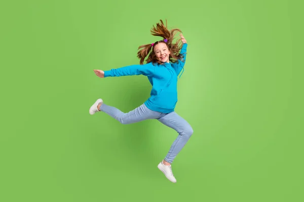 Foto panjang penuh gadis muda yang bahagia melompat mengenakan celana jeans terbang rambut menikmati waktu luang terisolasi pada latar belakang warna hijau — Stok Foto
