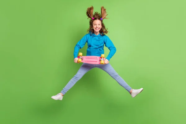 Фотографія повного тіла коричневого хвоста маленька дівчинка стрибає вгору муха волосся тримайте джинси з дошкою ізольовані на фоні зеленого кольору — стокове фото