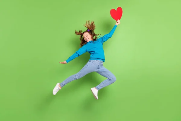Foto em tamanho completo de feliz morena cauda menina salto mosca cabelo segurar papel vermelho coração desgaste casual roupas isoladas no fundo de cor verde — Fotografia de Stock