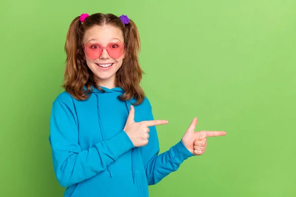 Фото позитивно приятно молодой девушки указывать пальцем пустое пространство улыбка солнцезащитные очки изолированы на зеленом фоне — стоковое фото