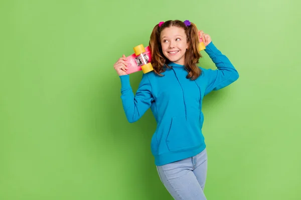 Foto von verträumten jungen glücklichen kleinen Mädchen aussehen leeren Raum Lächeln halten Schlittschuh isoliert auf grünem Hintergrund — Stockfoto