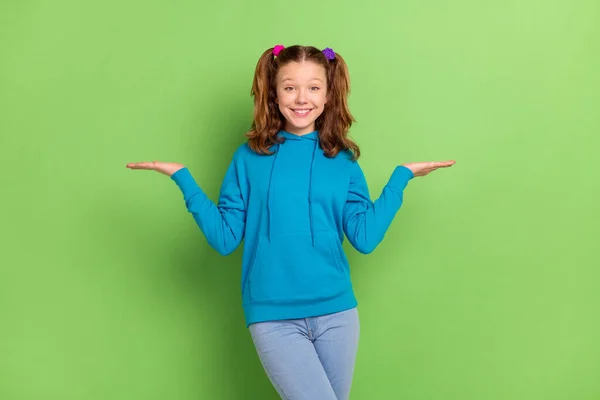 Foto van positieve gelukkig brunette staart harig klein meisje houd handen schalen copyspace geïsoleerd op groene kleur achtergrond — Stockfoto