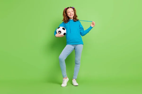 Lunghezza completa foto di allegra felice piccola ragazza tenere per mano il calcio guardare spazio vuoto isolato su sfondo di colore verde — Foto Stock
