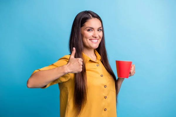 Foto retrato de la mujer bonita que muestra como signo de pulgar hacia arriba con taza de café en la rotura aislado en el fondo de color azul vibrante — Foto de Stock