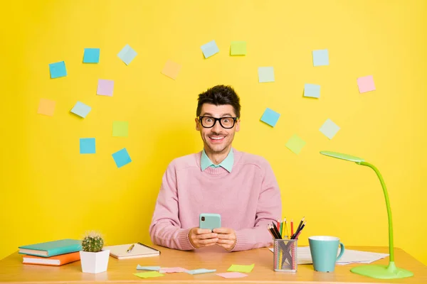 Fénykép a fiatal izgatott férfi boldog pozitív mosoly sit desk tanulmány használata mobiltelefon elszigetelt sárga színű háttér papír matricák — Stock Fotó