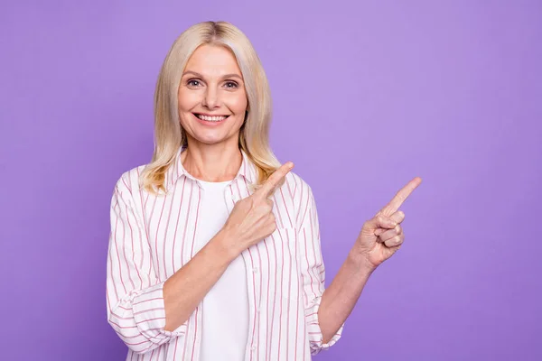 Foto de mulher madura muito doce vestido camisa rosa apontando dois dedos espaço vazio isolado cor roxa fundo — Fotografia de Stock