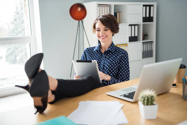 Фотопортрет деловой женщины, просматривающей интернет с планшетом, сидящей в офисе со шпильками на столе, смеющейся перед выходными — стоковое фото