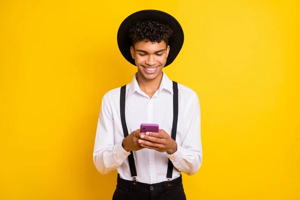 Foto van positieve man houden telefoon look scherm slijtage hoed wit shirt bretels geïsoleerde gele kleur achtergrond — Stockfoto