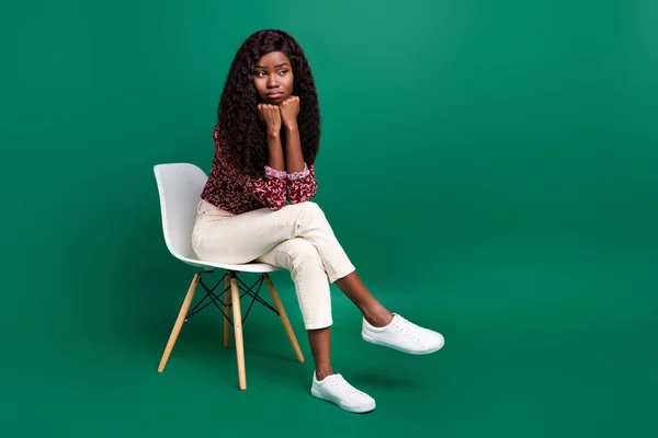 Foto de infeliz chateado ondulado pele escura senhora desgaste impressão camisa sentado cadeira braços queixo olhando espaço vazio isolado cor verde fundo — Fotografia de Stock