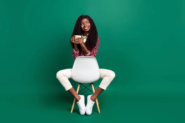 Foto de bonito sonhador encaracolado pele escura mulher vestida camisa sentado cadeira beber chá olhando espaço vazio isolado cor verde fundo — Fotografia de Stock