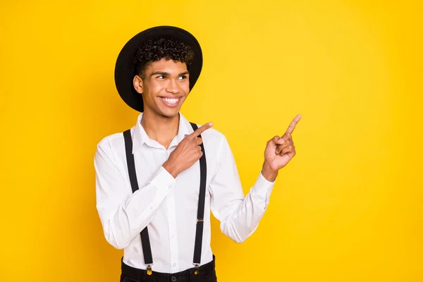 Фото промотор хлопець прямі пальці вгору дивитися порожній простір носити сорочки підтяжки капелюха ізольовані жовтого кольору фону — стокове фото