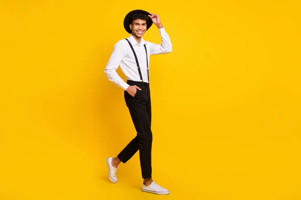 Foto av självsäker kille promenad titta kamera bära huvudbonad skjorta hängslen skor isolerad gul färg bakgrund — Stockfoto