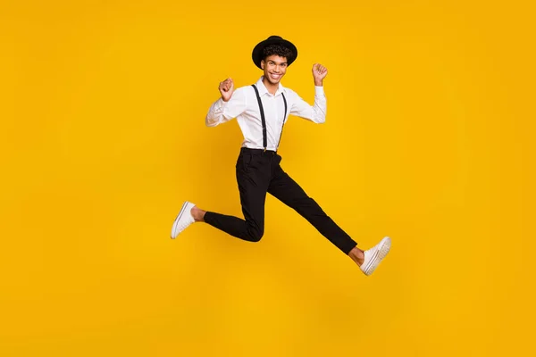 Foto de cara louco funky saltar levantar punhos usar headwear camisa suspensórios tênis isolado cor amarela fundo — Fotografia de Stock