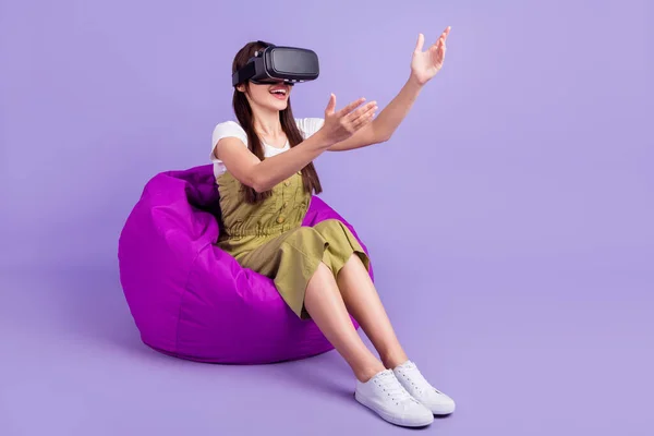 Full body photo of charming young pretty woman sit bean bag hands empty space vr game isolated on violet color background — Stock Photo, Image