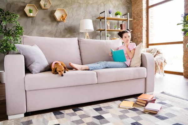 Portrait von attraktiven Geist verträumt preteen Mädchen Buch lesen bleiben allein mit Hündchen sitzen auf dem Sofa im hellen Haus drinnen — Stockfoto