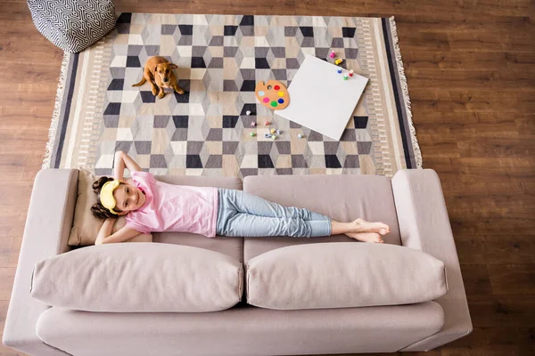 Oben über dem Hochwinkelbild Porträt eines attraktiven, fröhlichen Mädchens, das mit Hund in der Freizeit zu Hause auf dem Sofa liegt — Stockfoto