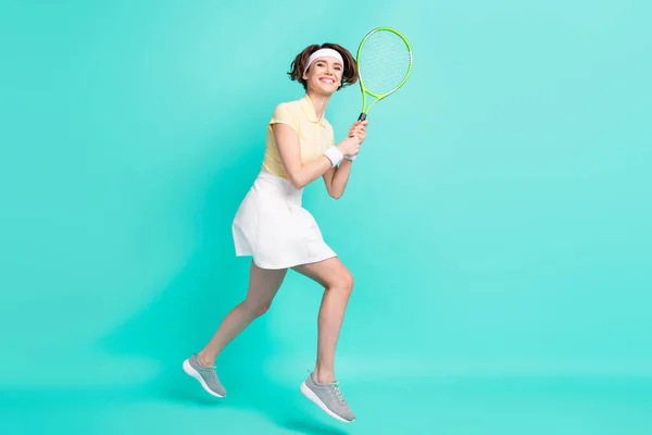 Foto em tamanho completo de feliz sorrindo positivo menina pulando jogando tênis badminton isolado no fundo cor turquesa — Fotografia de Stock