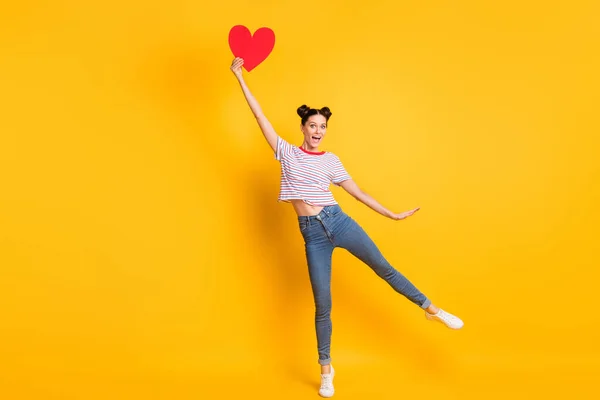 Foto de excitada encantadora joven dama usar camiseta a rayas sosteniendo gran corazón rojo aislado color amarillo fondo — Foto de Stock