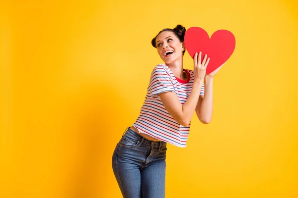 Foto de sonho engraçado menina vestida listrado t-shirt segurando vermelho papel coração olhando lugar vazio isolado cor amarela fundo — Fotografia de Stock