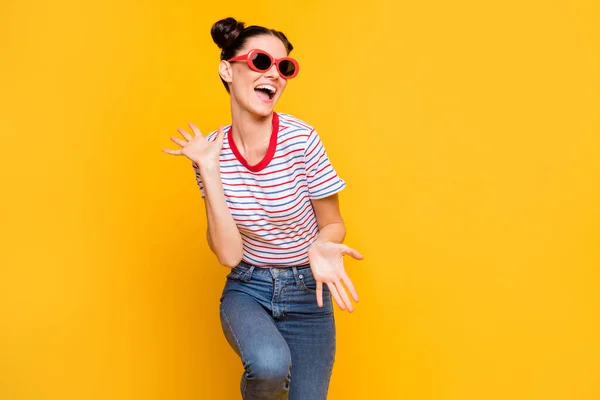 Foto di affascinante bella giovane donna indossare a strisce t-shirt occhiali scuri ballando braccia spazio vuoto isolato colore giallo sfondo — Foto Stock