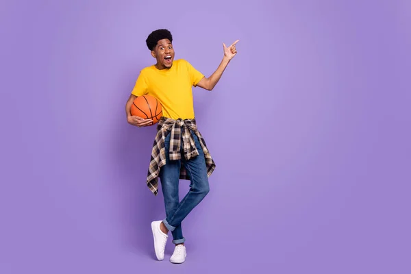 Corpo inteiro foto de jovem afro-americano desgaste jeans jeans apontar dedo vazio espaço basquete isolado na cor violeta fundo — Fotografia de Stock