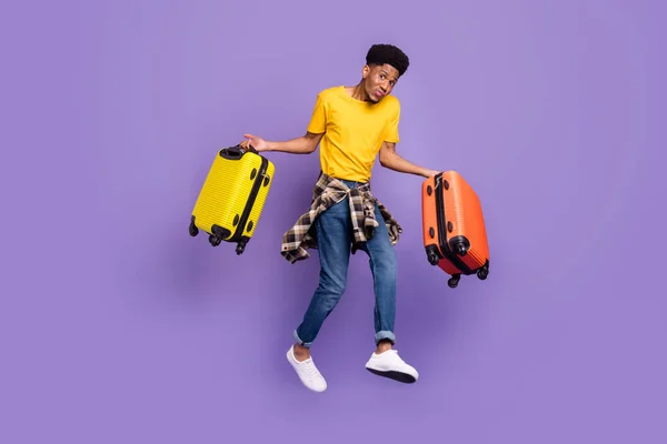 Plná délka tělo velikost pohled na atraktivní zmatený chlap skákání nesoucí zavazadla v zahraničí izolované přes fialové fialové barvy pozadí — Stock fotografie