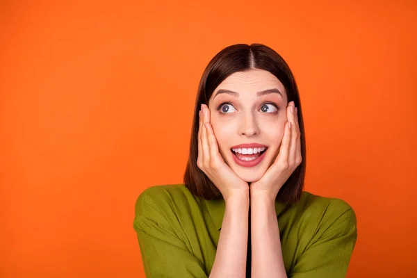 Foto de la fresca morena peinado milenial dama manos mejillas mirada espacio vacío desgaste camisa de color caqui aislado sobre fondo de color naranja — Foto de Stock