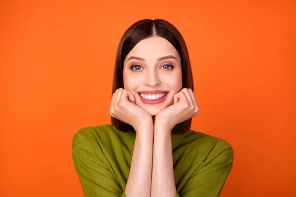 Foto de bonita morena penteado milenar senhora mãos bochechas usar camisa verde isolado no fundo cor de laranja — Fotografia de Stock