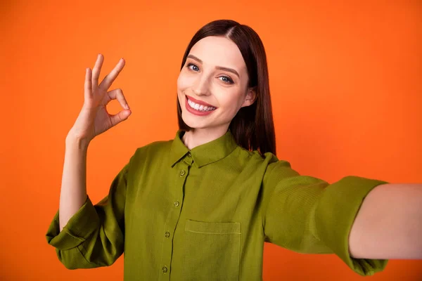 Foto de la divertida morena peinado joven dama hacer selfie show okey desgaste camisa verde aislado sobre fondo de color naranja —  Fotos de Stock