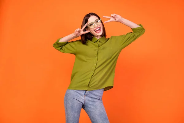 Foto de louco morena penteado jovem senhora mostrar v-sign desgaste specatcles camisa verde isolado no fundo cor de laranja — Fotografia de Stock