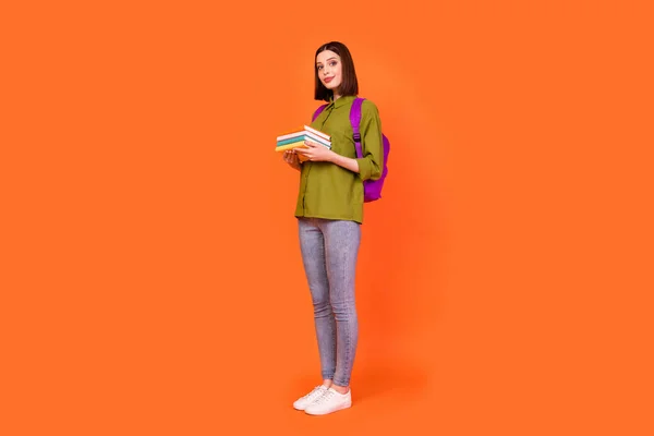 Full body foto di carino bruna millenaria signora stand tenere libri usura borsa camicia jeans isolato su sfondo di colore arancione — Foto Stock