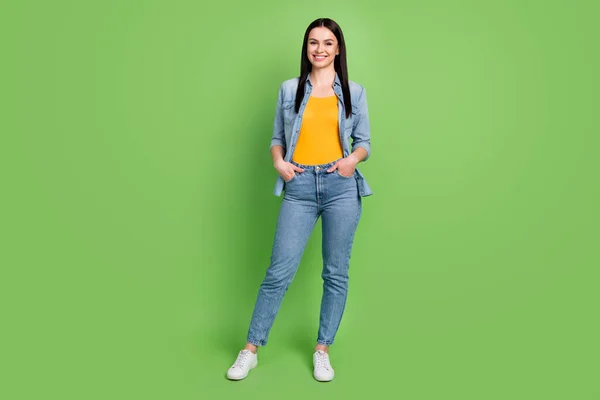 Full storlek foto av ung vacker glad kvinna bära jeans denim hålla händerna fickor isolerade på grön färg bakgrund — Stockfoto