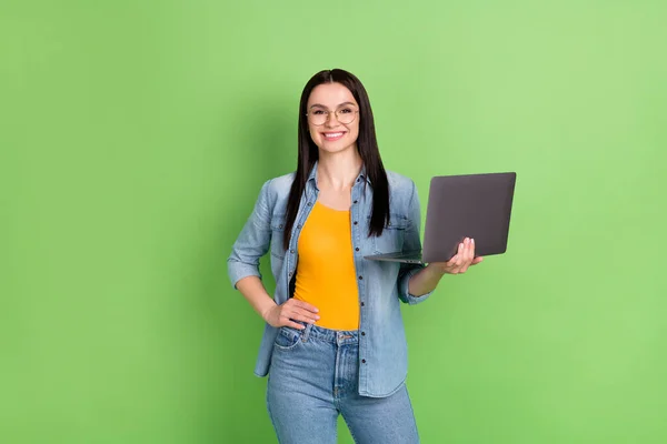 Foto de positivo muito marrom penteado senhora segurar laptop desgaste óculos jeans camisa laranja top isolado no fundo de cor verde — Fotografia de Stock