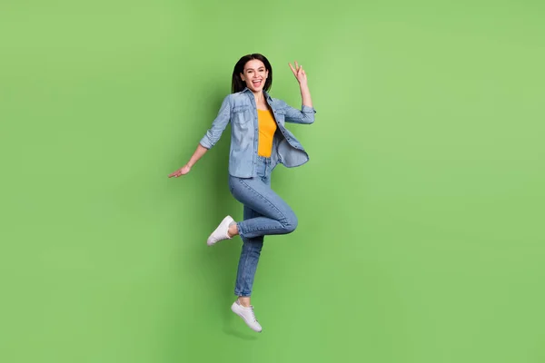Foto de perfil de longitud completa de divertido lindo pelo marrón señora salto espectáculo v-signo de desgaste jeans camisa aislada en pastel verde fondo de color —  Fotos de Stock