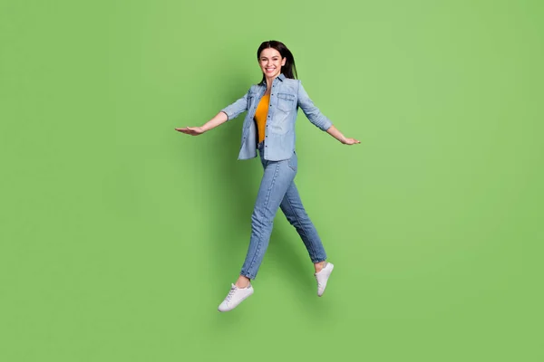 Full length profiel foto van vrolijke mooie bruine kapsel dame springen dragen jeans shirt geïsoleerd op pastel groene kleur achtergrond — Stockfoto