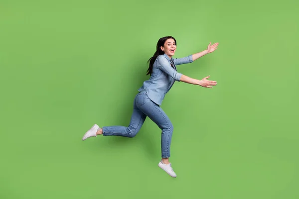 Full size profil fotografie legrační hnědý účes dáma spustit nosit džíny košile tenisky izolované na pastelové zelené barvy pozadí — Stock fotografie