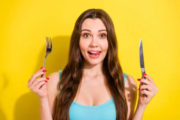 Photo portrait girl wearing blue singlet smiling hungry keeping fork knife licking lips isolated bright yellow color background