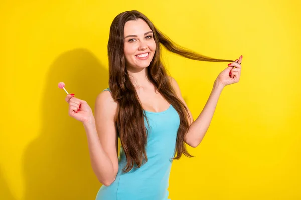 Фотопортрет девушка в синем сингле улыбаясь держать леденец касаясь волос изолированы ярко-желтый цвет фона — стоковое фото