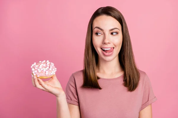 Foto de bonito complicado jovem mulher vestida roupas casuais segurando olhando donut lambendo lábios isolado cor-de-rosa fundo — Fotografia de Stock