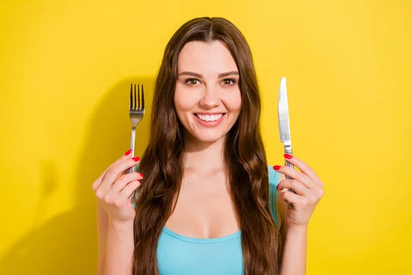 Foto retrato menina vestindo azul singlet sorrindo com fome mantendo faca garfo isolado vibrante cor amarela fundo — Fotografia de Stock