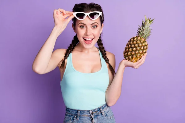 Portrait of attractive cheerful girl touching specs holding in hand juicy ananas isolated over violet purple color background — ストック写真