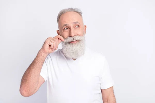 Portrait of positive grey hair old man look empty space touch beard wear white t-shirt isolated on grey color background — ストック写真